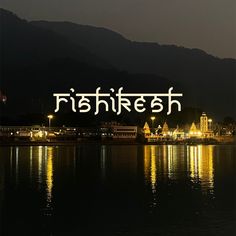 the words are lit up in front of a lake with buildings and mountains behind it