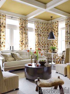 a living room filled with lots of furniture next to two large windows covered in curtains