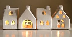 three small white houses are lit up with candles