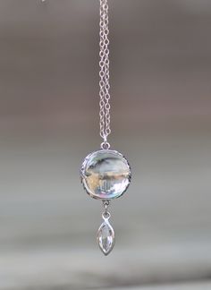 "A truly stunning, art deco era pools of light necklace. This one is made with an un-drilled rock crystal orb. It is bezeled in sterling silver with amazing floral detail. Orb measures 15mm around and connects to a marquise shaped channel set crystal. I love the detail to this one! The crystal is exceptional quality, with no major imperfections inside the jewel. Note how the crystal makes the images shining through flip upside down and backwards! Pendant hangs from sterling silver chain that is Elegant Drop Glass Jewelry, Elegant Drop-shaped Glass Jewelry, Elegant Glass Drop Jewelry, Unique Round White Gold Necklaces, Art Deco White Gold Oval Necklace, Art Deco White Gold Gemstone Necklace, White Gold Art Deco Gemstone Necklace, Art Deco White Gold Necklace With Gemstone, Elegant Glass Jewelry With Cabochon