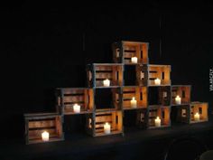 several wooden crates with lit candles on them in the dark, set against a black wall