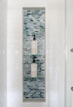 a white bathroom with two glass shelves holding soap and lotion bottles on the wall