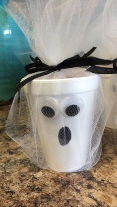 two white cups decorated like ghost faces with tulle and black ribbon on top, sitting on a marble countertop