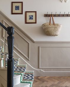 there is a basket hanging on the wall next to some stairs with pictures above it