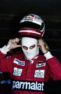 a man wearing a white mask and red racing suit is covering his face with one hand