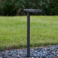 a black metal post in the middle of some rocks and grass with trees in the background