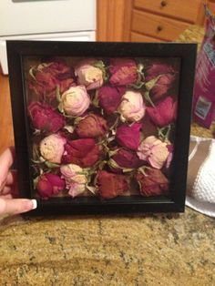 a person holding up a frame with flowers in it on a counter top next to a microwave