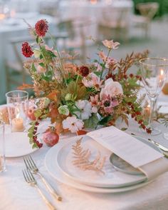 the table is set with white plates and silverware, floral centerpieces, and candles