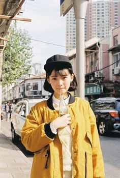 a woman standing on the sidewalk with a drink in her hand and wearing a hat