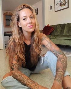 a woman with tattoos sitting on the floor in front of a couch and looking at the camera