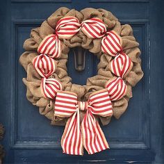 a wreath with red and white striped bows hanging on a blue front door, decorated with burlap