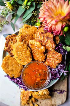 a plate full of fried food with sauce on the side and flowers in the background