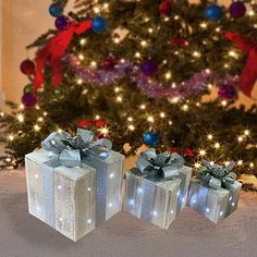 three wrapped presents sitting in front of a christmas tree with lights and decorations on it