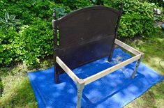 a bed frame sitting on top of a blue mat in front of some bushes and trees