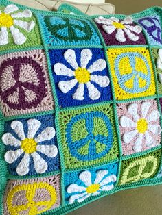 a crocheted pillow with flowers and peace signs on the front is sitting on a couch