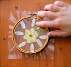 a hand is holding a needle and an embroidered flower on a piece of clear plastic