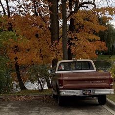 a truck parked on the side of a road next to trees with leaves turning yellow