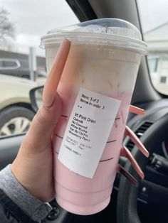 a person holding up a pink drink in their hand while sitting in the driver's seat