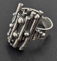 Artisan Signed Sterling Silver Abstract Modernist Brutalist 3-D Statement Ring Circa 1960s Size: 7.5-US / 55-EU / K 1/2-UK Band: .25"W (.64cm) Face: 1"L x .75"W x .25"H (2.54cm x 1.91cm x .64cm) Markings: ST925 Weighs: 13.4g Crafted by an expert artisan, this vintage sterling silver 3-D statement ring is truly a statement piece. With it's abstract brutalist design and oxidized recesses, this ring exudes a sense of edgy sophistication. Made with premium quality sterling silver, it's a timeless addition to any jewelry collection. Luxury Hand Cast Modernist Jewelry, Luxury Brutalist Ring Jewelry, Hand Cast Metal Brutalist Jewelry, Brutalist Jewelry, Luxury Brutalist Metal Jewelry, Luxury Collectible Brutalist Jewelry, Silver Brutalist Hand-cast Rings, Brutalist Design, Modernist Jewelry