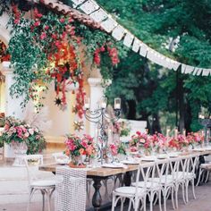 a long table with white chairs and pink flowers on it is surrounded by greenery