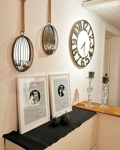 three framed pictures are hanging on the wall next to a clock and vases with flowers in them