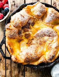 a baked pastry with powdered sugar on top and berries in the bowl next to it