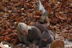 a woman laying on the ground next to a child with her feet up in leaves