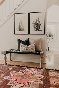 two paintings on the wall above a bench in a room with wooden floors and stairs