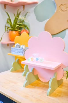 a wooden table topped with pink and yellow furniture next to potted plants on shelves