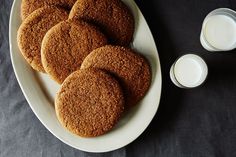 six cookies on a white plate next to two glasses of milk