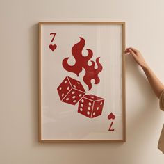 a woman is holding up a framed print with two dices on it and flames coming out of the back