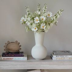 a white vase sitting on top of a wooden table next to books and a plant