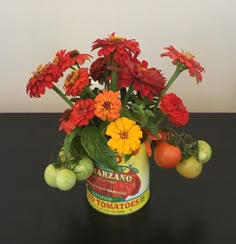 an arrangement of flowers in a can on a table with tomatoes and other fruit around it