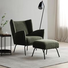 a green chair and footstool in a white room with a black floor lamp