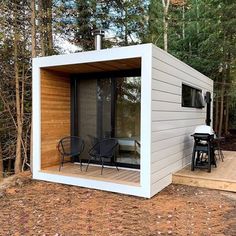 a small house built into the side of a wooded area with chairs and an outside table