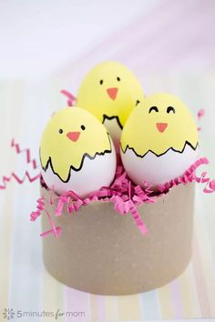 three decorated eggs in a cardboard container on a striped tablecloth with pink streamers