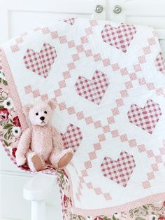 a pink teddy bear sitting on top of a chair next to a quilted heart