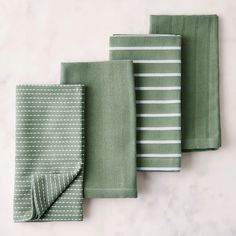 four folded green and white napkins on a marble countertop, with one folded in half