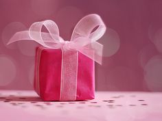 a red gift box with a white ribbon and bow sitting on top of a table