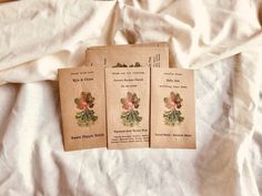 three old - fashioned seed packets sitting on top of a white bed sheet with flowers