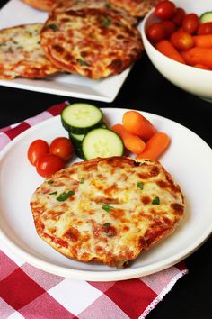 two plates with pizza, cucumbers and carrots on them next to some other food