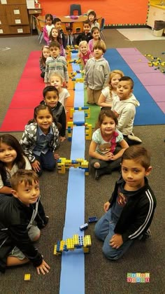 a group of children sitting on the floor in front of a train track with legos