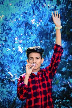 a young boy is holding his hand up in the air while wearing a red and black checkered shirt