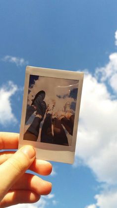 someone holding up a polaroid with the sky and clouds in the backgroud