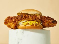 a fried chicken sandwich sitting on top of a white marble slab with mustard and ketchup