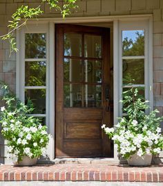 two planters with white flowers are on the front step of a house, next to a wooden door