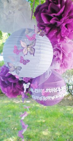 purple and white paper lanterns hanging from a tree in the grass with butterflies on them