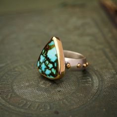 The Sonoran Gold Turquoise is on a 7mm wide sterling silver band, dotted with 18k yellow gold studs. More 18k gold wraps around a beautiful, triangle-shaped piece of Turquoise from Mexico. The face of the ring measures ~3/4" across at the widest point and ~7/8" down. This ring is a size 7.5 Keep in mind, when choosing a wider ring band, you will need to size up between a half to three quarters of a size from what you might be used to. The wider the band, the more you'll need to size up. Each ring is one-of-a-kind, handmade in our Boulder, Colorado jewelry studio and an excellent choice for everything from bridal jewelry to daily wear. Not exactly what you're looking for? Check out our customs page. Raw Turquoise Ring, Gold Turquoise Ring, Raw Turquoise, Turquoise Gold Ring, Gold Wrap, Boulder Colorado, Wide Rings, Wide Band Rings, Jewelry Studio