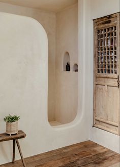 a wooden bench sitting in front of a white wall with an arched window next to it