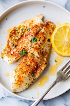 a white plate topped with fish next to a slice of lemon